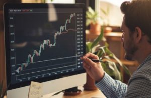 A man examines a computer screen displaying a stock chart, surrounded by financial tools and investment options.